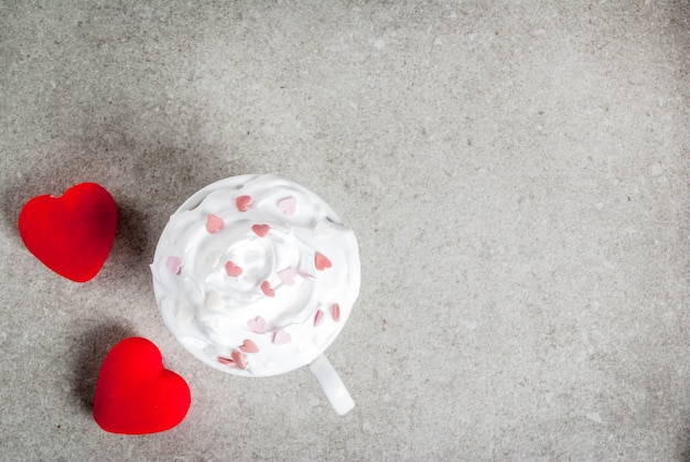 Romantico, San Valentino. Tazza per caffè o cioccolata calda, con panna montata e cuori dolci, con due cuori rossi peluche, vista dall'alto