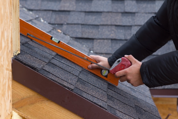 Roofer che tiene un metro a nastro e una livella tra le mani su piastrelle appena installate su una casa in legno di nuova costruzione