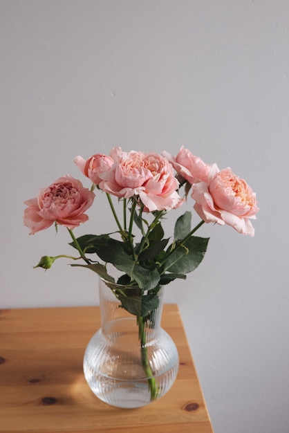 Rosa rosa in vaso sul tavolo di legno sul muro grigio verticale