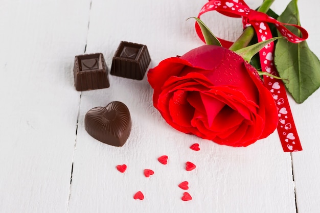 Rosa rossa, cioccolato su un fondo di legno bianco