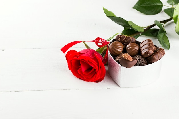 Rosa rossa, scatola di cioccolatini su un fondo di legno bianco