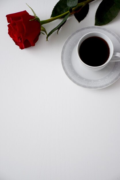 Rosa rossa, tazza di caffè sul piatto del set da tè grigio sul tavolo bianco. Carta di San Valentino