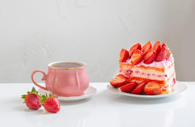 Rosa tazza di caffè e torta di fragole su sfondo bianco