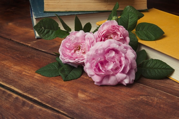 Rose e libro rosa con una copertina gialla su un fondo di legno. Il concetto di storie e romanzi romantici