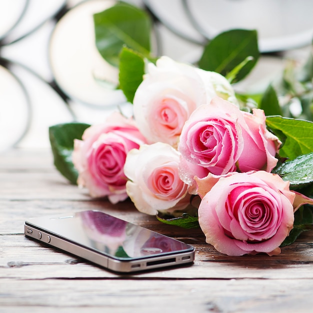 Rose e smartphone rosa sulla tavola di legno