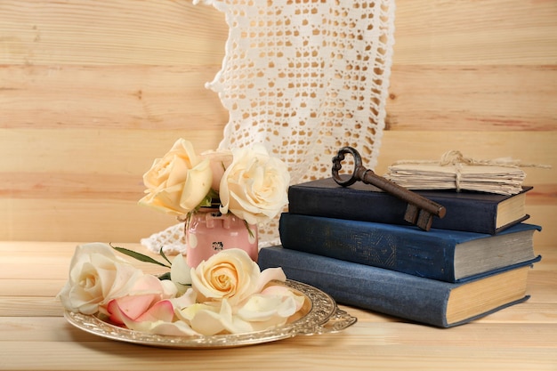 Rose fresche con il vecchio libro, la chiave e le lettere sul fondo della tavola di legno. Concetto d'epoca