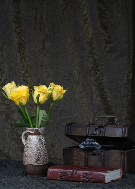 Rose gialle in un vaso su uno sfondo di tessuto scuro una vecchia cassa di legno un libro in pelle un diamante