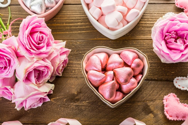 Rose rosa con cioccolatini su tavola in legno rustico.