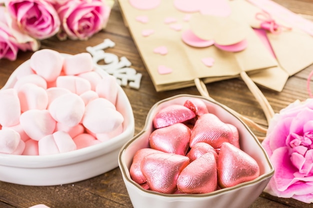 Rose rosa con cioccolatini su tavola in legno rustico.