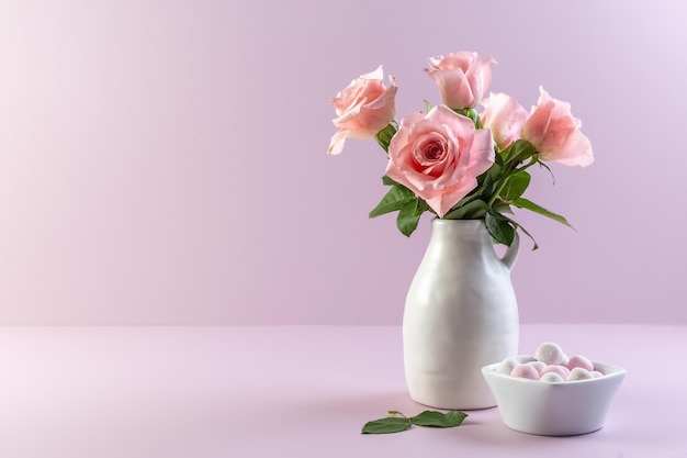 Rose rosa in un vaso di ceramica bianca e caramelle rotonde in un vaso su uno sfondo viola Spazio per la copia della carta