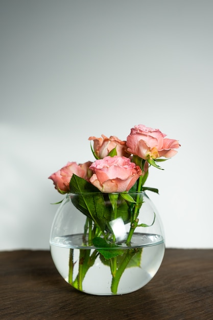 rose rosa in un vaso tondo trasparente su un tavolo di legno