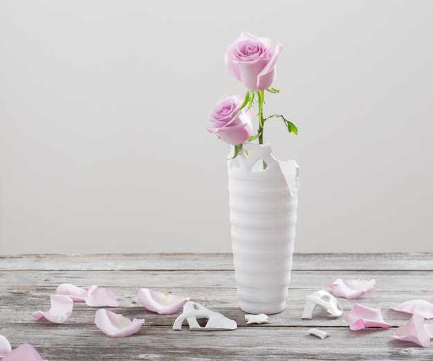 Rose rosa in vaso di fiori rotto sulla vecchia tavola di legno