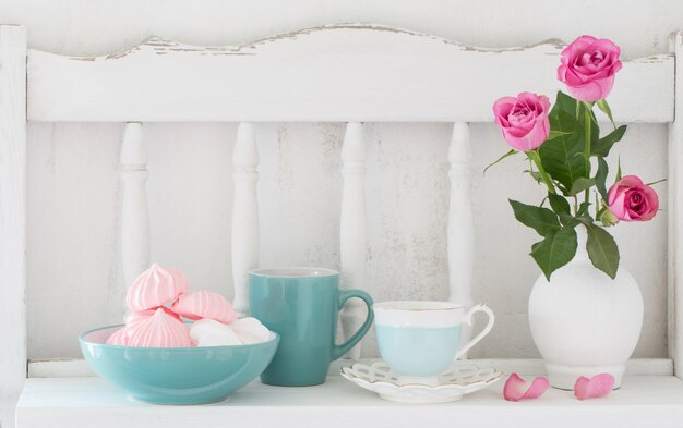Rose rosa in vaso e stoviglie sullo scaffale di legno bianco