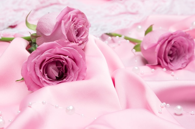 Rose rosa su tessuto di seta piegato con filo di perline bianche. Sfondo romantico con fiori