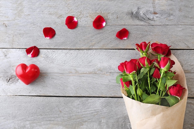 Rose rosse avvolte in carta con cuori su sfondo tavolo in legno