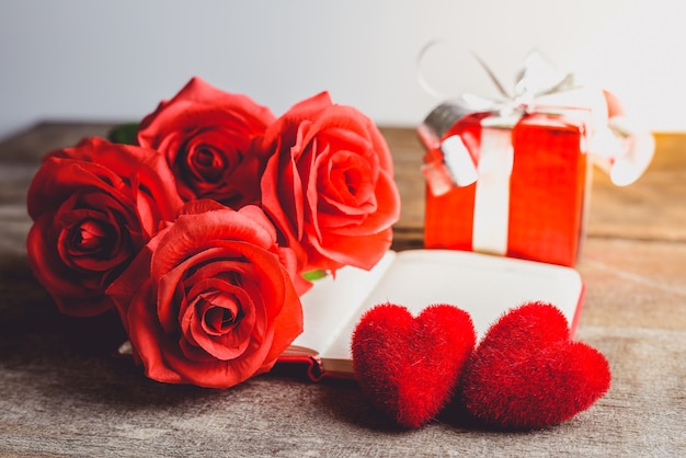 Rose rosse, cuore rosso, taccuino e contenitore di regalo su un fondo di legno