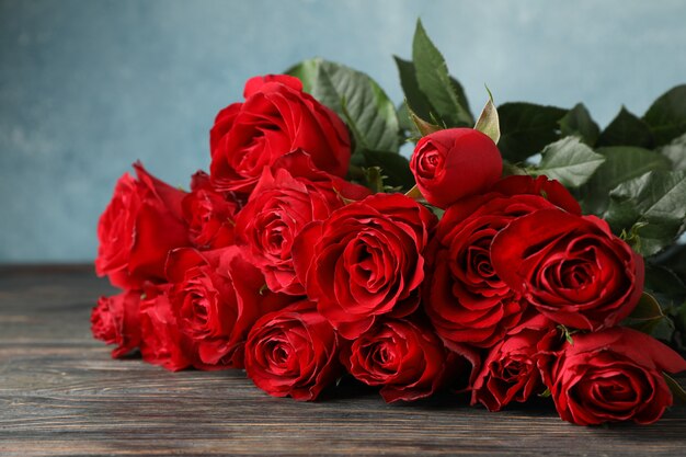 Rose rosse del mazzo sulla tavola di legno contro la fine blu della tavola su