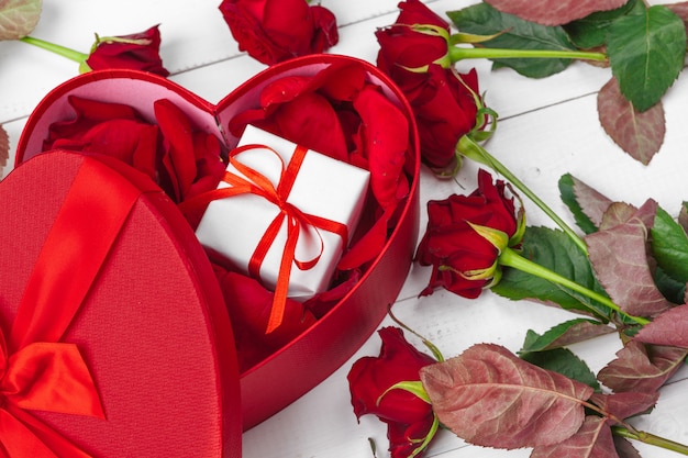 Rose rosse e contenitore di regalo sulla tavola di legno