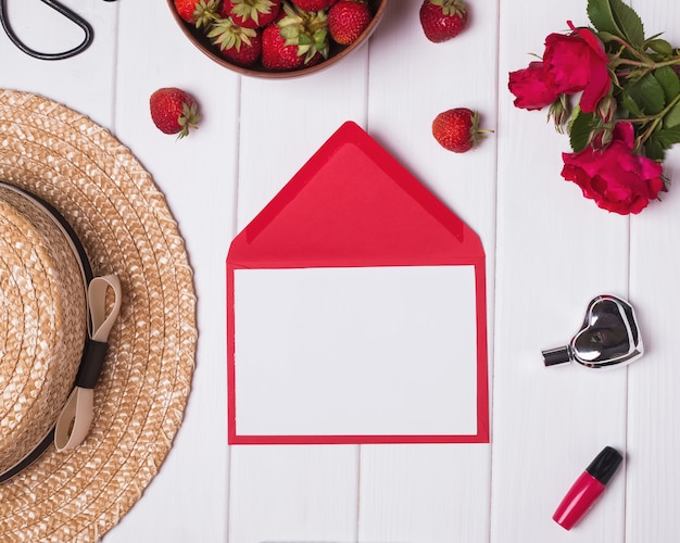 Rose rosse e fragole del cappello della carta in bianco su fondo di legno bianco Concetto di estate