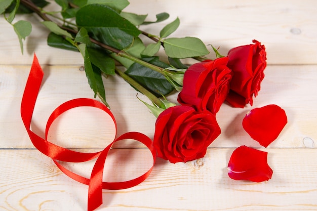 Rose rosse e nastro su un tavolo in legno chiaro. San Valentino. Vista dall'alto con copia spazio