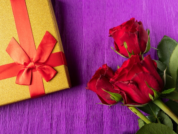 Rose rosse e regalo giallo con nastro rosso su viola