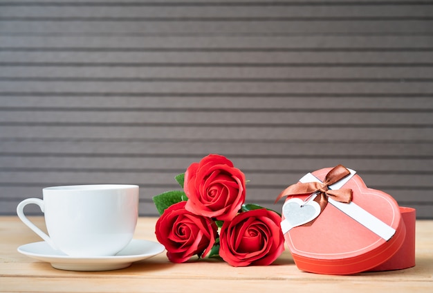Rose rosse e scatola regalo su fondo di legno