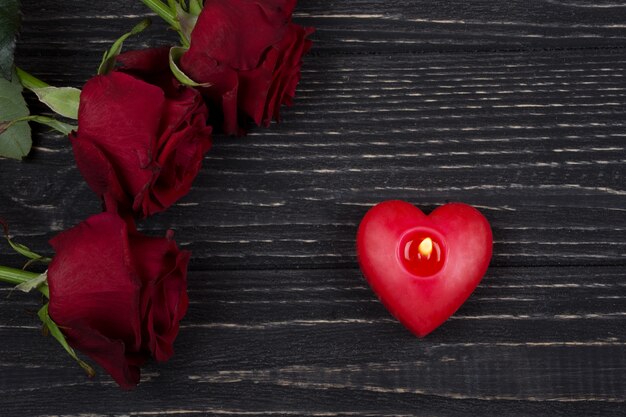 Rose rosse e una candela a forma di cuore rossa