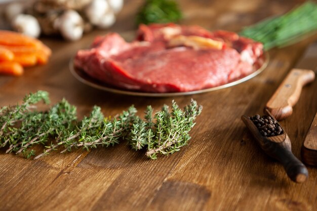 Rosmarino verde davanti a due pezzi di carne rossa accanto a verdure fresche e coltello da chef. Erbe verdi. Carne gustosa.