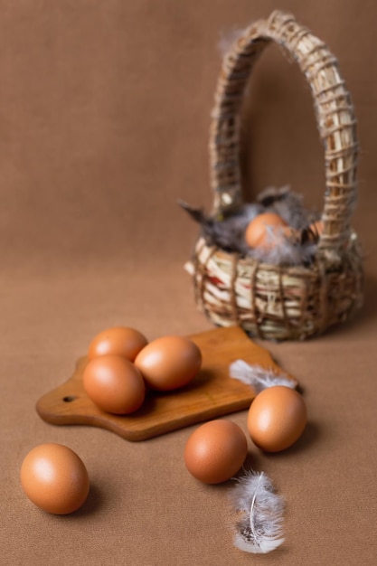 Rosolare le uova in un cesto su uno sfondo marrone con una tavola di legno e un cesto con una piuma.