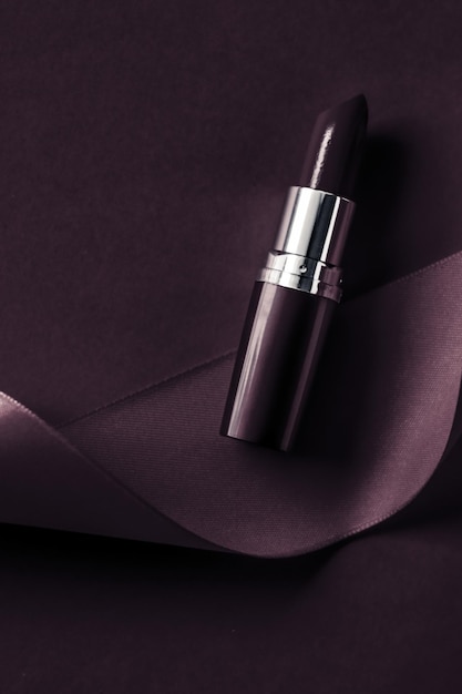 Rossetto di lusso e nastro di seta su sfondo viola scuro per le vacanze trucco e cosmetici flatlay per il design di prodotti di marca di bellezza