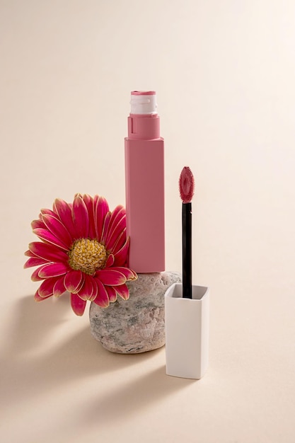 Rossetto liquido rosa e pennello applicatore con fiori e pietra Prodotto cosmetico per il trucco Sfondo luminoso