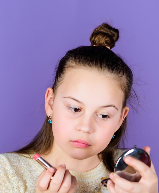 Rossetto per una lucentezza unica. Adorabile bambina che applica il colore del rossetto. Piccolo bambino sveglio con il tubo del rossetto che guarda in vetro. Modello di bellezza con rossetto premuroso per le sue labbra.