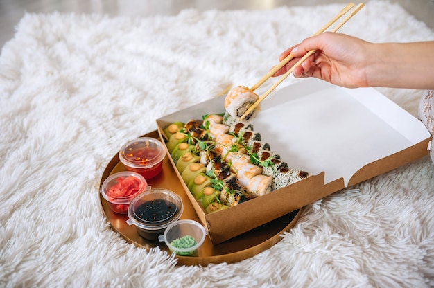 Rotolare nella mano della ragazza sullo sfondo di un vassoio con sushi.