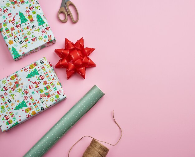 Rotoli con carta da regalo, corda marrone, forbici, decorazioni e una scatola quadrata avvolta con un regalo