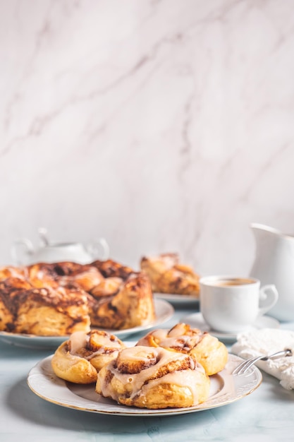 Rotoli di cannella fatti in casa su un piatto bianco su un tavolo bianco con caffè e focacce per la colazione