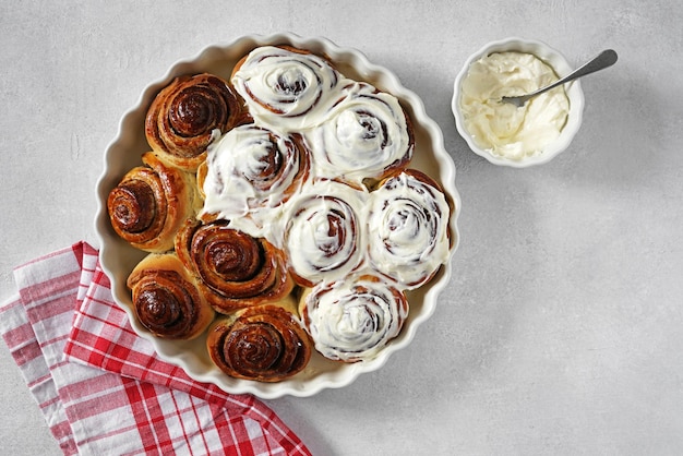 Rotoli di cannella o cinnabon dolci fatti in casa tradizionali panini da dessert con salsa di panna bianca su sfondo grigio bianco copia spazio vista dall'alto