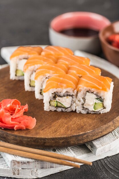 Rotoli di sushi classici Philadelphia su una tavola di legno con zenzero, salsa di soia e bacchette su una superficie scura