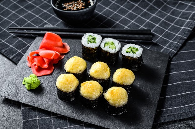 Rotoli di sushi con cetriolo, salmone e gamberi su un vassoio di pietra. Superficie nera. Vista dall'alto