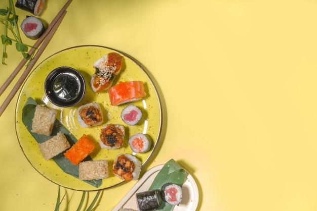 Rotoli di sushi con riso e pesce, salsa di soia e bacchette su sfondo giallo, flatlay alla moda alla luce del giorno