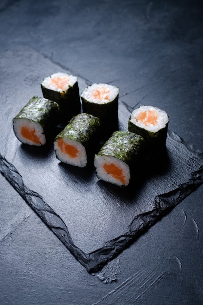 Rotoli di sushi con salmone ricoperto di nori su sfondo scuro. Menu ristorante di cucina orientale. Cibo tradizionale delizioso