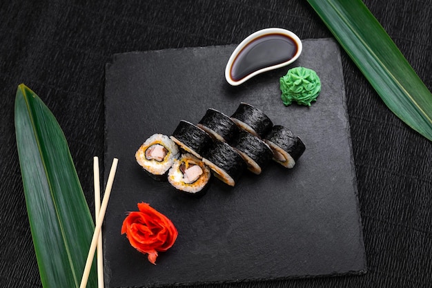 Rotoli di sushi disposti su uno sfondo scuro decorato con foglie di bambù e bacchette