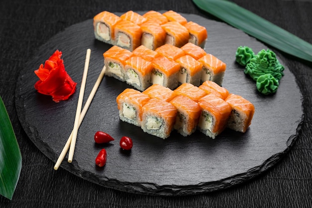 Rotoli di sushi disposti su uno sfondo scuro decorato con foglie di bambù e bacchette