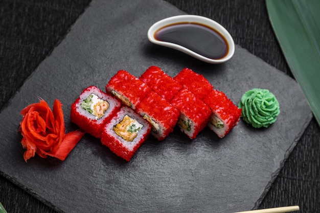 Rotoli di sushi disposti su uno sfondo scuro decorato con foglie di bambù e bacchette