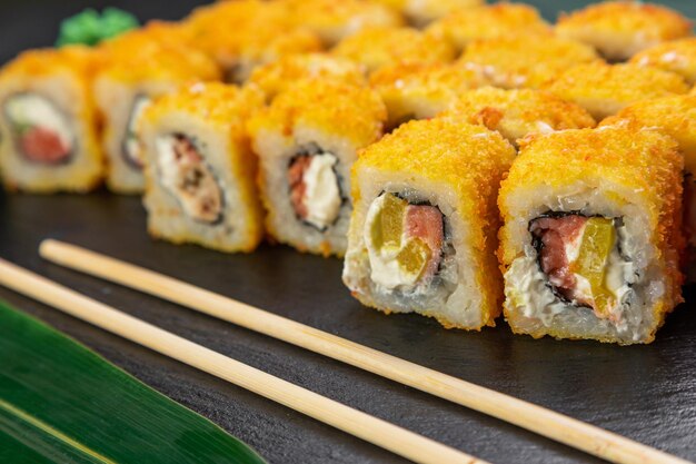 Rotoli di sushi disposti su uno sfondo scuro decorato con foglie di bambù e bacchette