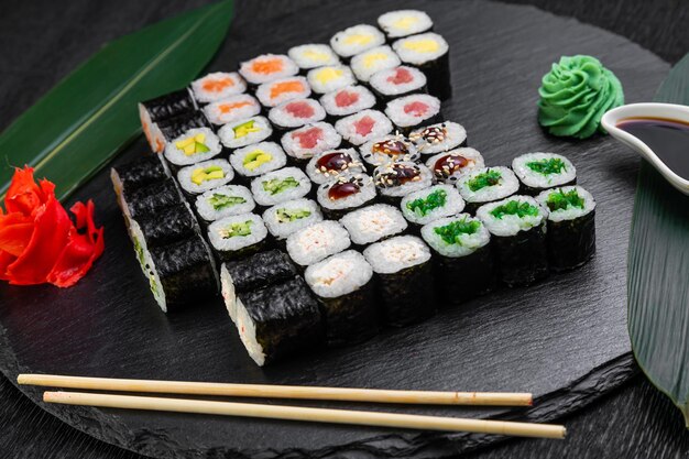 Rotoli di sushi disposti su uno sfondo scuro decorato con foglie di bambù e bacchette