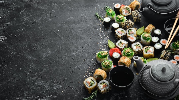 Rotoli di sushi e teiera con tè su sfondo di pietra nera Grande set di cibo giapponese