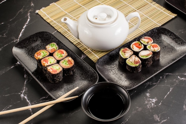 Rotoli di sushi freschi e gustosi con bastoncini e salsa su sfondo nero