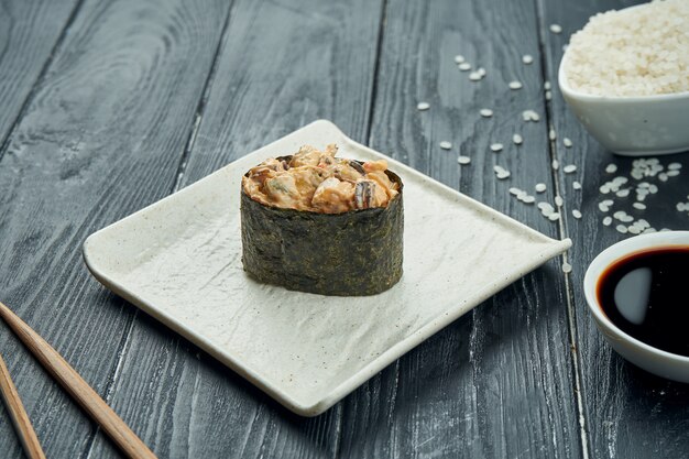 Rotoli di sushi giapponesi classici - gunkan con le cozze e la salsa bianca piccante su un piatto ceramico bianco su un fondo di legno nero. Avvicinamento