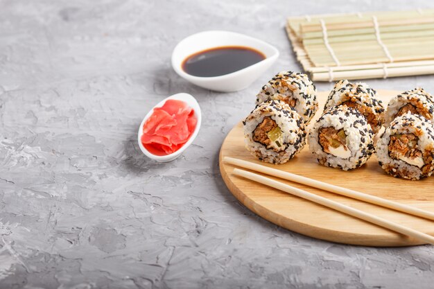 Rotoli di sushi giapponesi di maki con il cetriolo di sesamo di color salmone sul bordo di legno su un fondo concreto grigio