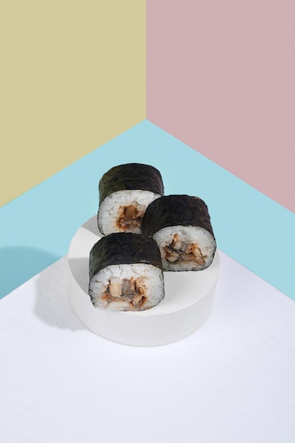 Rotoli di sushi Hosomaki con anguilla su un supporto in gesso bianco su uno sfondo colorato blu rosa giallo